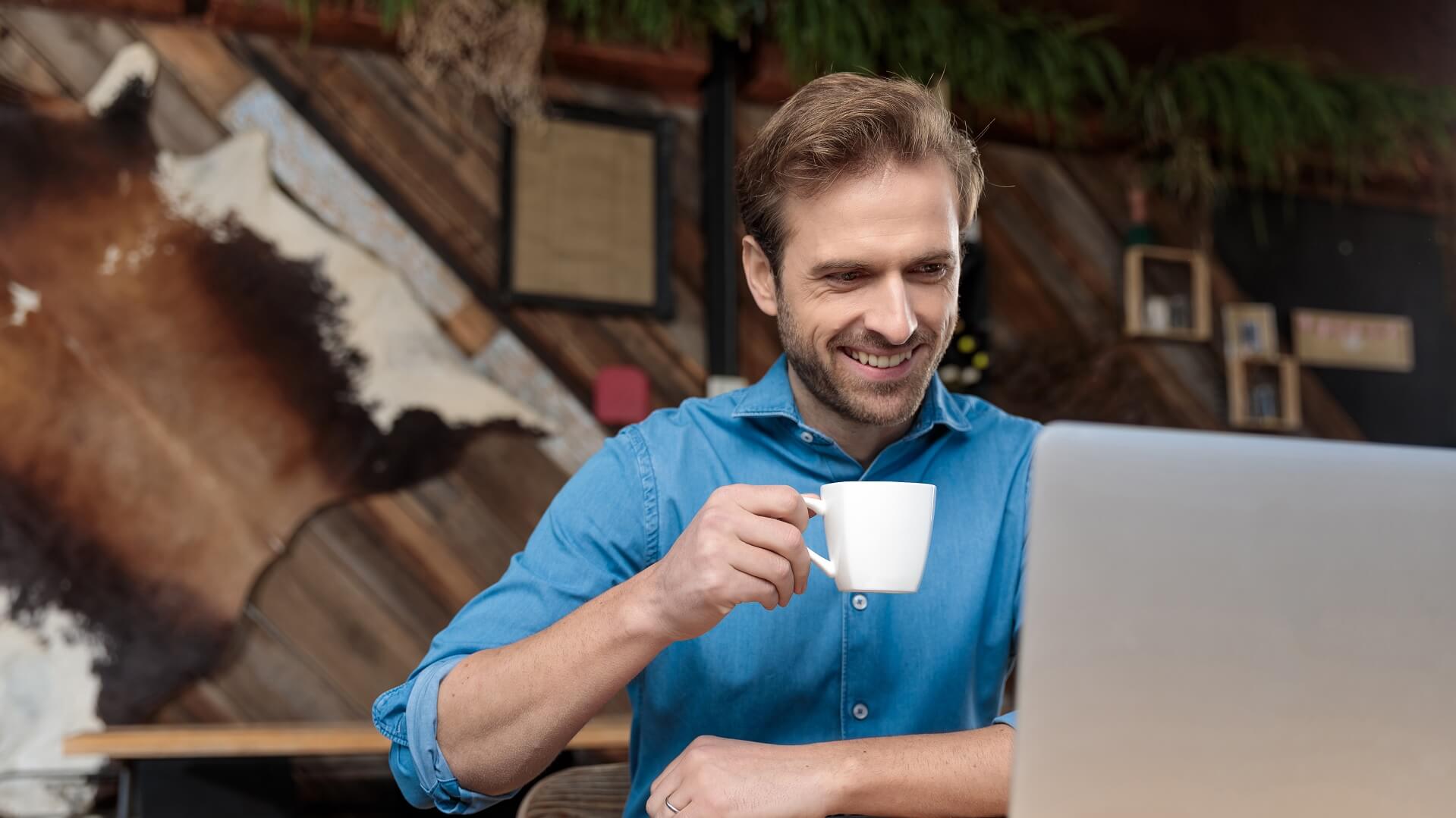 Ein lächelnder Geschäftsmann arbeitet am Laptop und trinkt Cappuccino