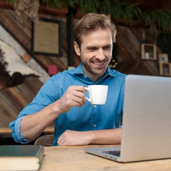 Ein lächelnder Geschäftsmann arbeitet am Laptop und trinkt Cappuccino